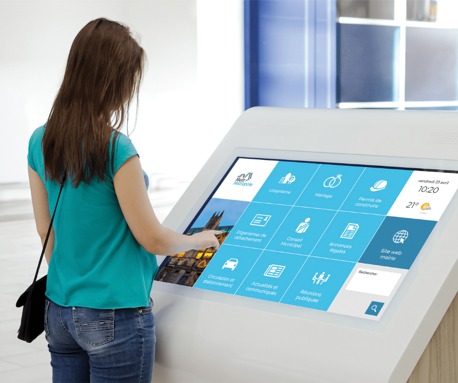 Image d'une femme utilisant une borne interactive pour accéder aux services d'une institution.