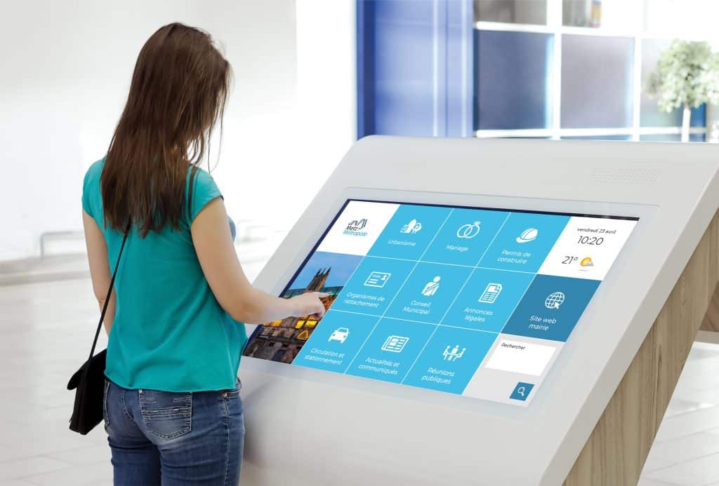 Image d'une femme utilisant une borne interactive TVTools pour affichage legal.